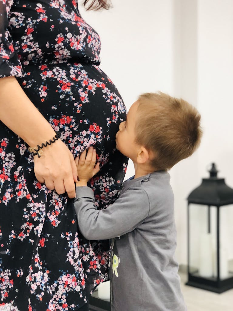 A touching scene of a young boy kissing his pregnant mother's belly indoors, symbolizing love and family bonds.